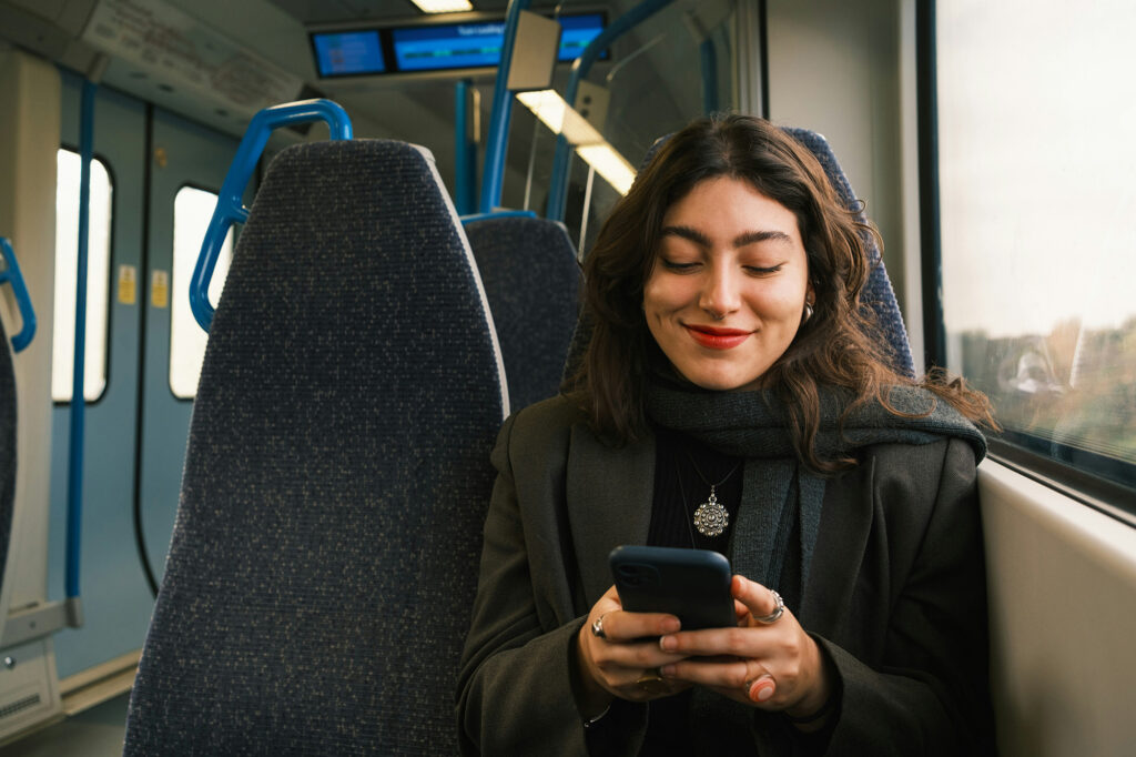 Eine Frau sitzt in der Straßenbahn und schaut lächelnd auf ihr Handy